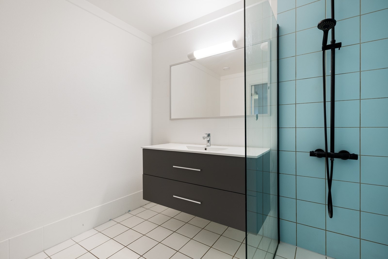 Bad med fliser på gulv med varmekabler. Fliser i dusjsone. Moderne baderomsinnredning og dusjvegg i glass. Galleribilde