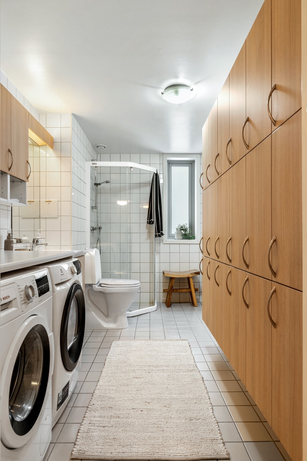 Badet er flislagt med lyse fliser på både gulv og vegger, noe som gir et rent og tidløst uttrykk. Rommet har en praktisk og romslig utforming med gode oppbevaringsmuligheter.
Badet er utstyrt med dusjhjørne med glassvegger og toalett. Det er opplegg for v Galleribilde