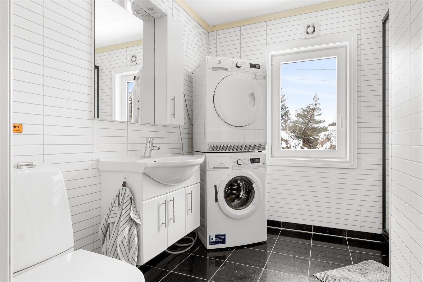 Baderommet inneholder servantmøbel, speil, gulvstående toalett, opplegg for vaskemaskin og dusjkabinett. Galleribilde