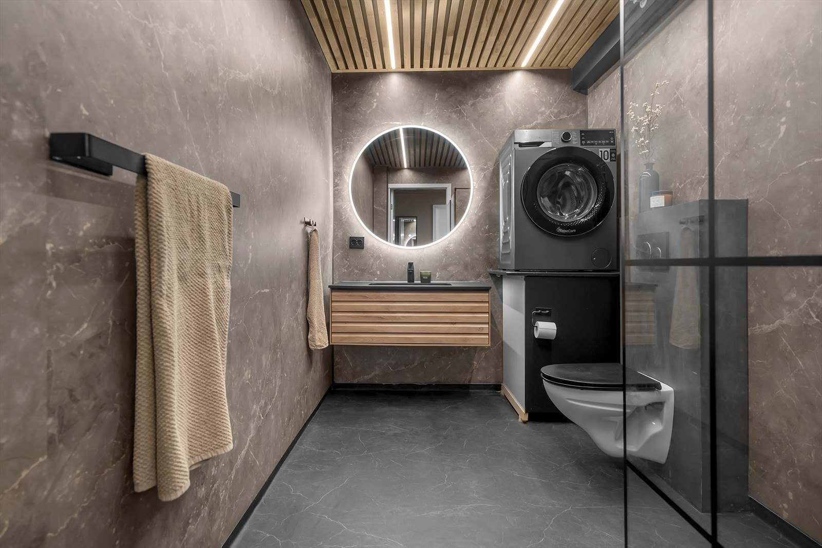 Lekkert bad med vegghengt toalett, servant med innredning og opplegg til vaskemaskin Galleribilde