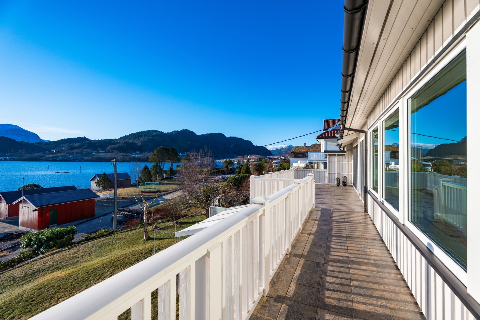 Mot syd er det langsgående terrasse med flislagt dekke. Legg merke til det koselige nabolaget med naust, eneboliger og hager. Galleribilde