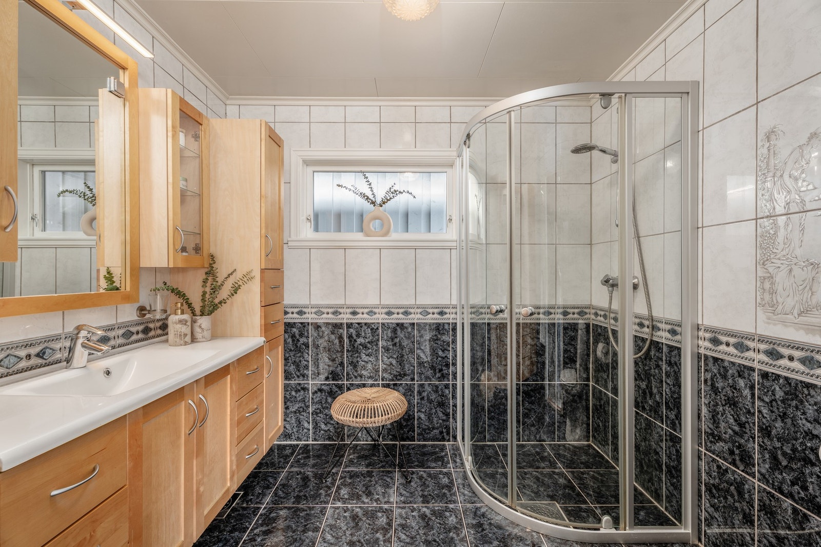 På badet er det innholdsrik servantinnredning med bøkefronter, flislagte gulv og vegger, dusjhjørne og WC. Galleribilde