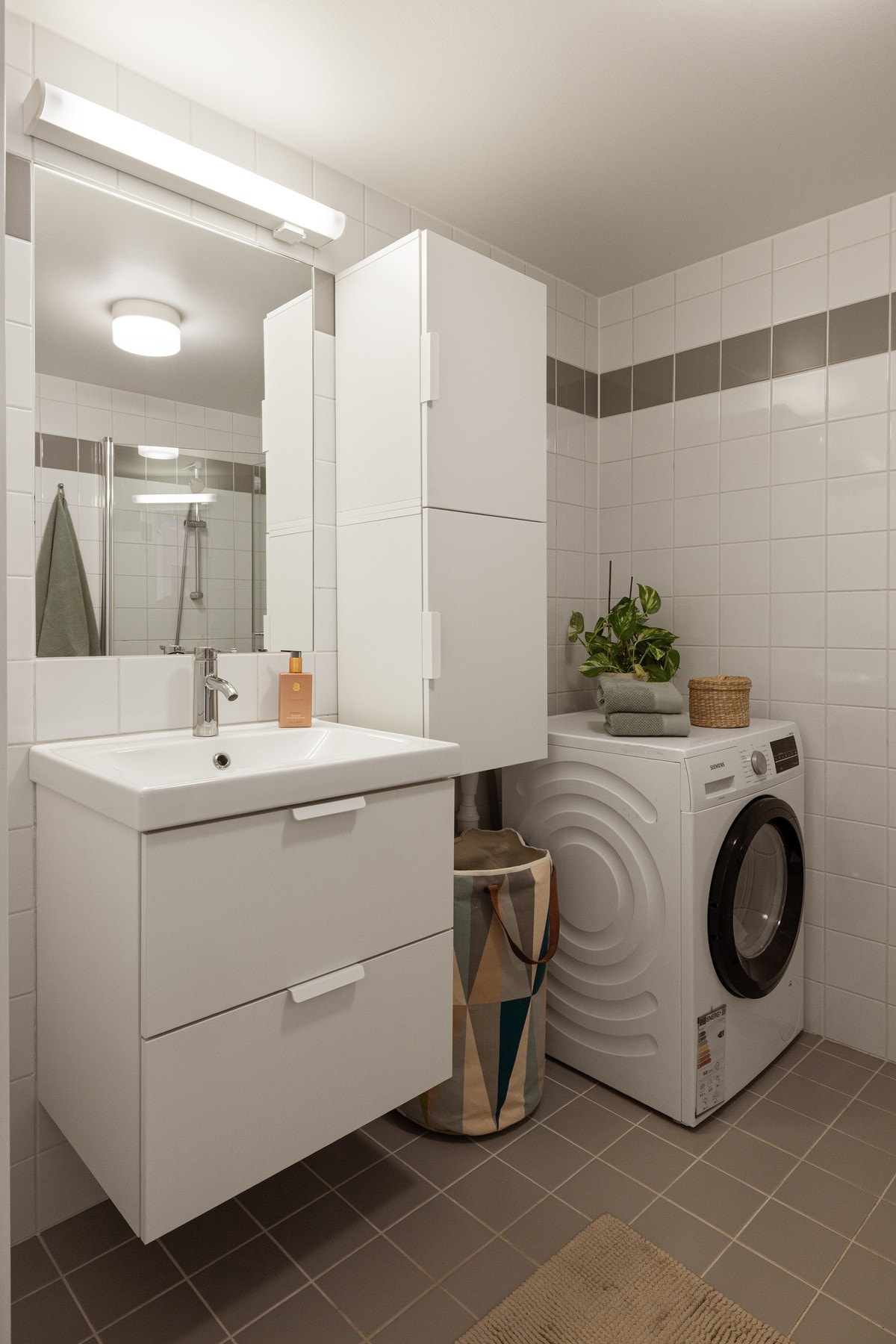 Lys baderomsinnredning med skuffer og heldekkende servant, speil med beysning over og vegghengt skap ved siden av. Galleribilde