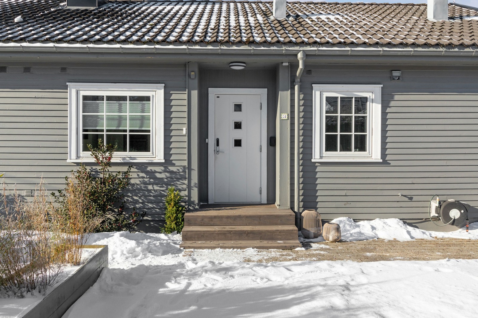 Inngangspartiet er inntrukket, og en hvit ytterdør med glassfelt og elektrisk kodelås fører inn i boligen. Galleribilde