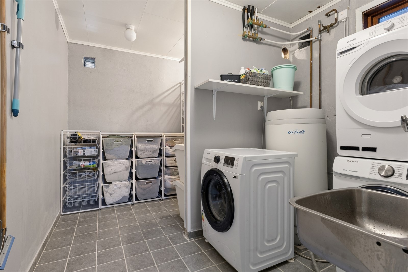 Praktisk vaskerom med flislagt gulv, malte plater og murpuss på vegger. Rommet er utstyrt med kum og har avløp for vaskemaskin. Ventilasjon ivaretas av to ventiler i vegg. Galleribilde