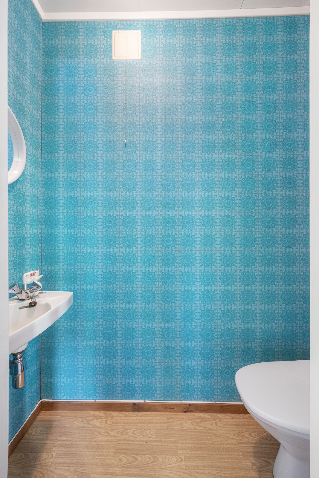 Wc-rommet har blå tapet på veggene og belegg i parkettimitasjon på gulvet. Galleribilde