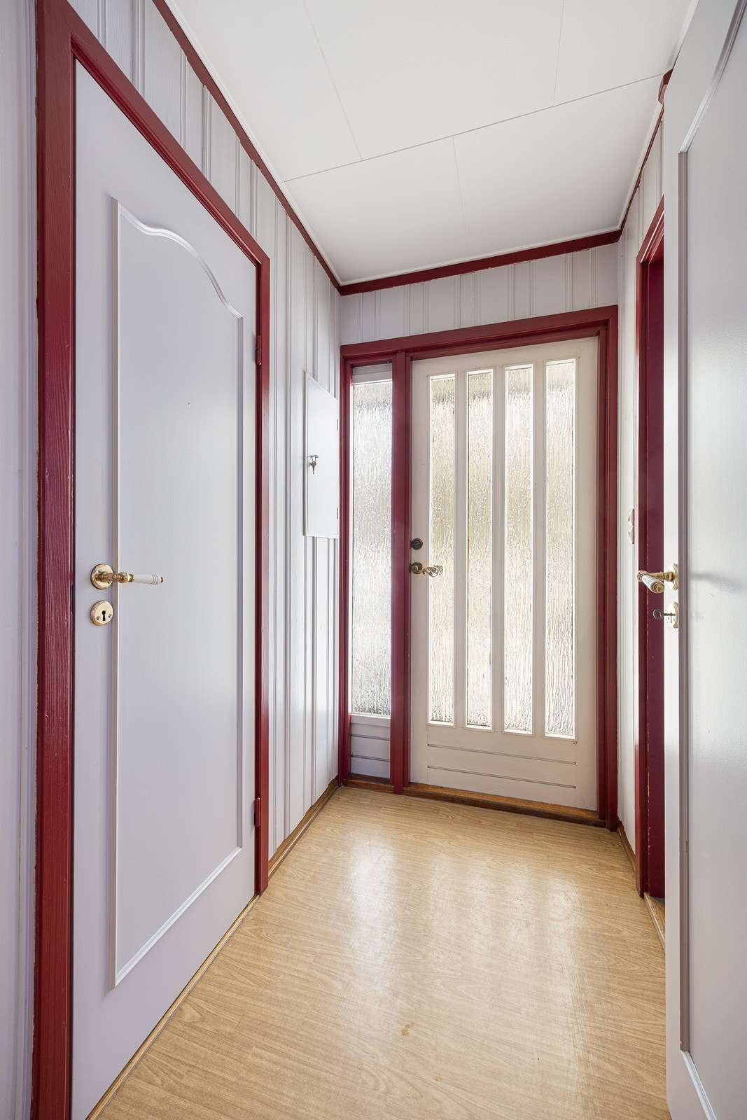 Vel inne er det en entré med lysmalt panel på veggene og belegg i parkettimitasjon på gulvet. Galleribilde