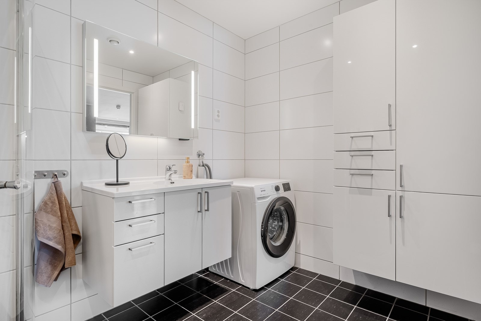 Flislagt bad med romslig innredning, dusjhjørne, vegghengt toalett og opplegg for vaskemaskin. Galleribilde