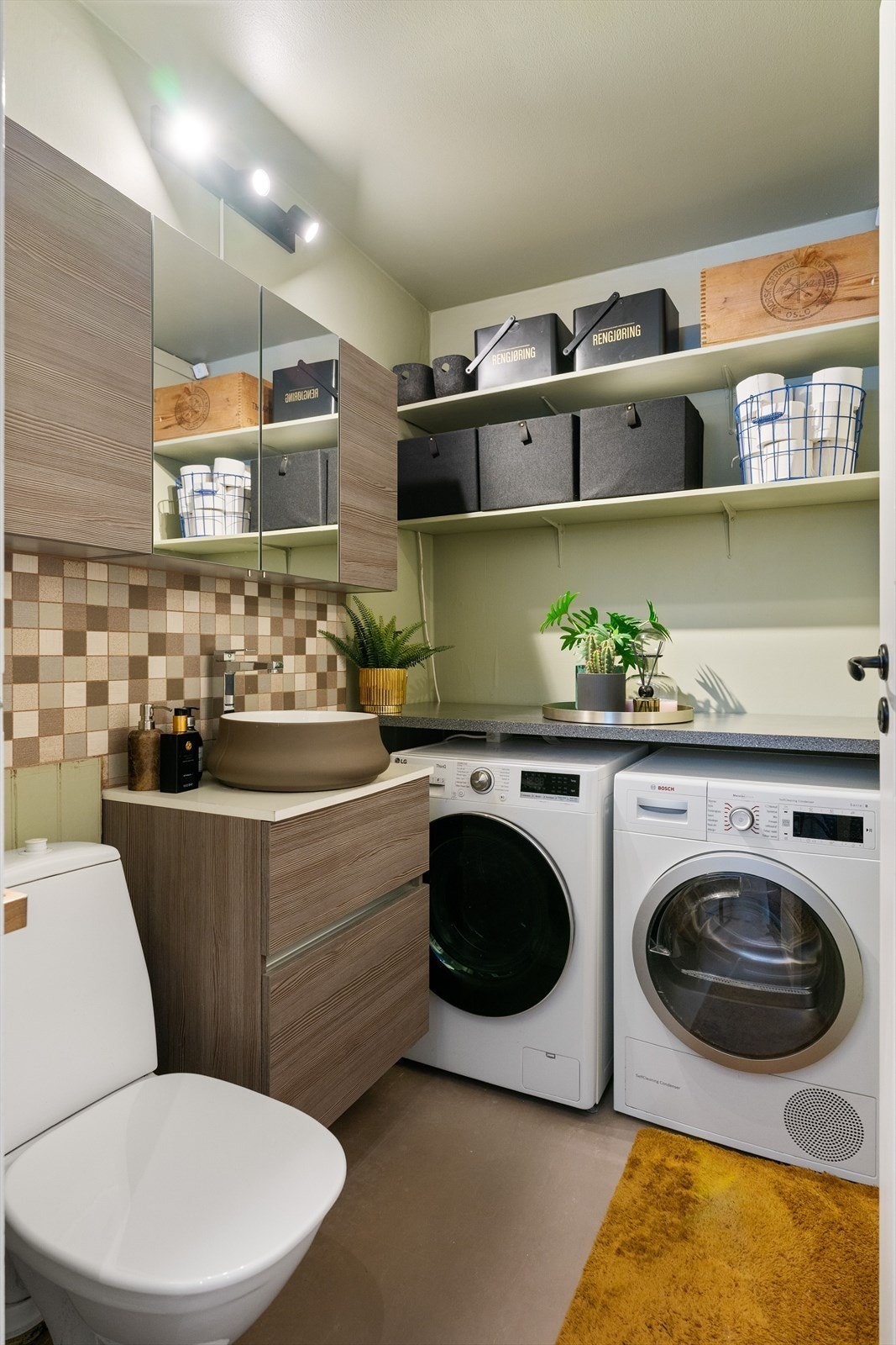 Vaskerommet har god plass til både vaskemaskin og tørketrommel under en praktisk benkeplate. Rommet er utstyrt med hyller for oppbevaring og har ny innredning fra 2026. Galleribilde