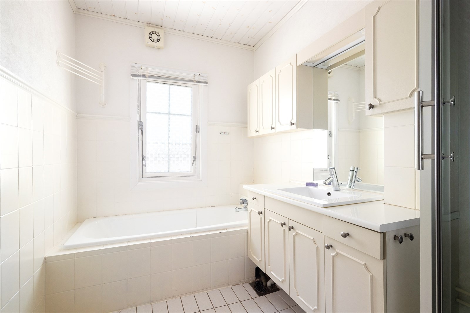 Badet har flislagt gulv med flis delvis opp på veggen. Badet er fra 80-tallet, med romslig innredning og innfliset badekar. Galleribilde