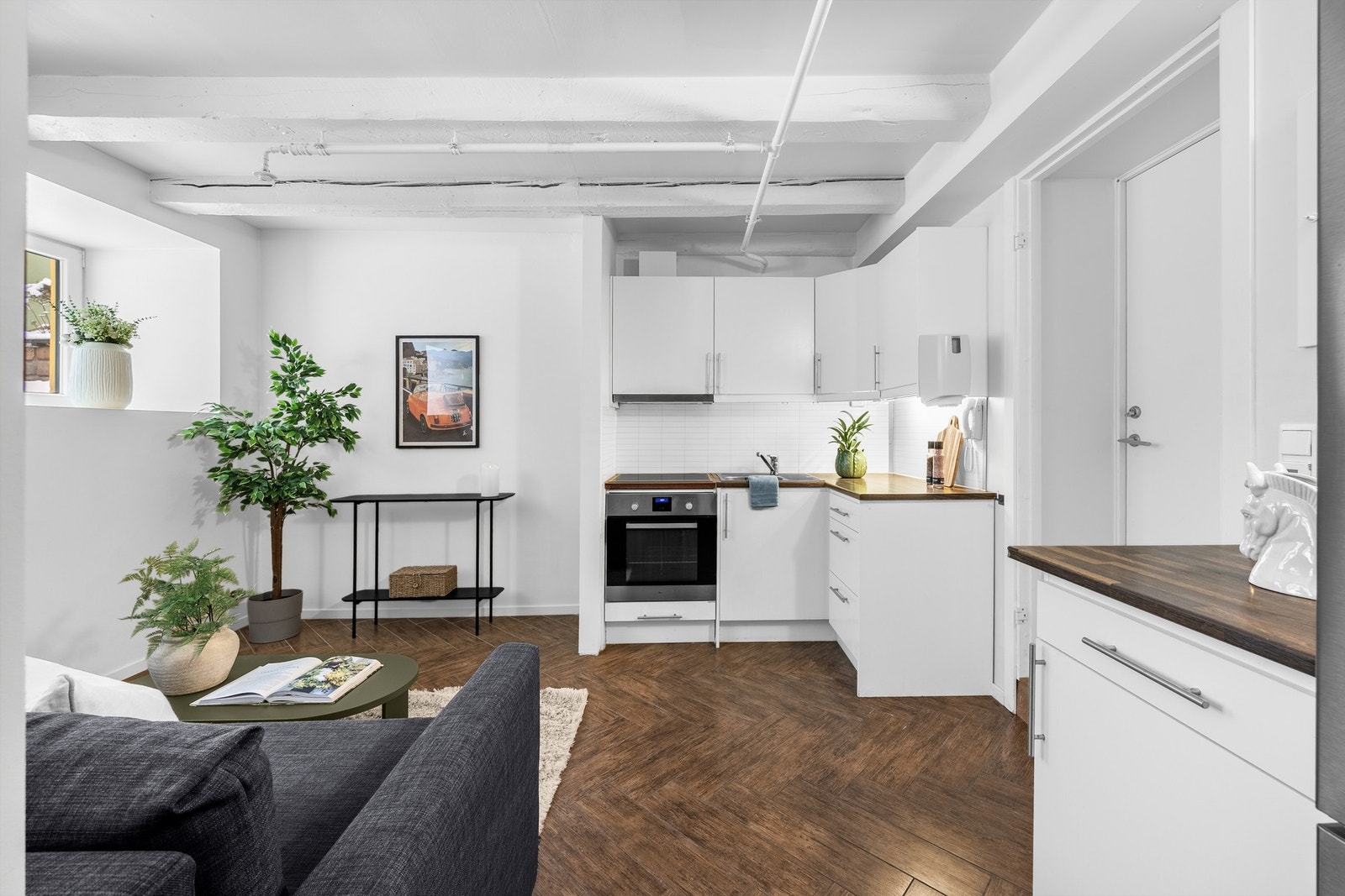 Et lite hjørnekjøkken bestående av hvite skapfronter, og laminat benkeplate. Galleribilde