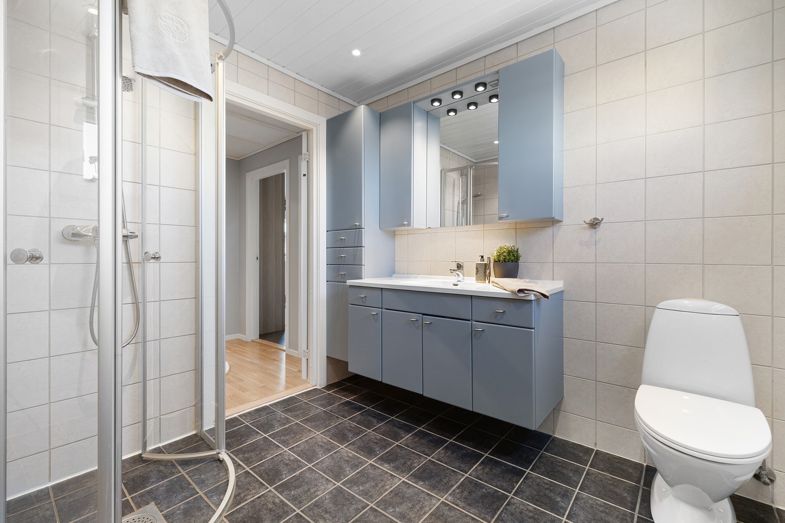 Her får du et dusjhjørne med innfellbare glassdører, toalett og servantskap i laminert glatt utførelse med heldekkende servantplate. Galleribilde