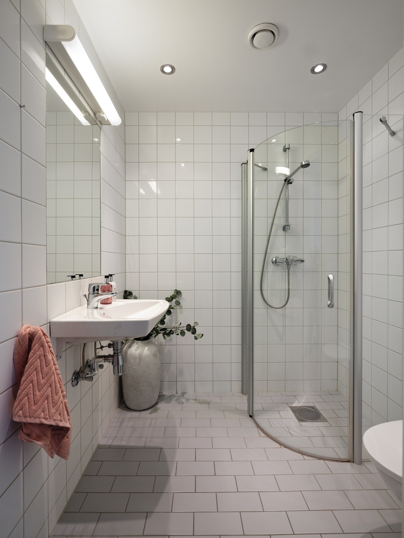 Flislagt baderom med servant, speil og belysning. Dusjløsning med buede glassvegger. Vegghengt toalett. Galleribilde