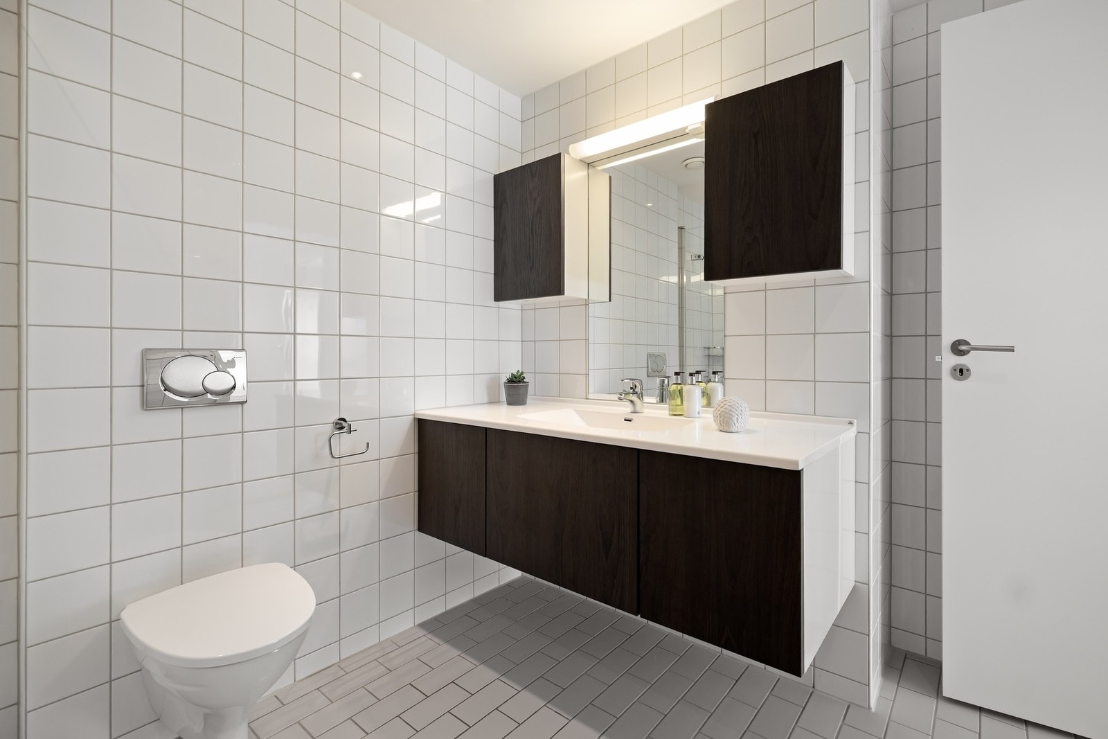 Flislagt baderom med servantinnredning med glatte fronter og helstøpt servantplate, speil, overskap og belysning. Galleribilde