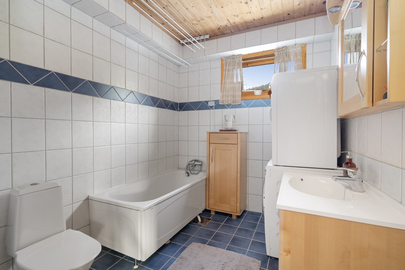 Pent baderom fra 2004 som inneholder heldekkende servant med underskap, overskap, toalett, badekar og opplegg til vaskemaskin. Galleribilde