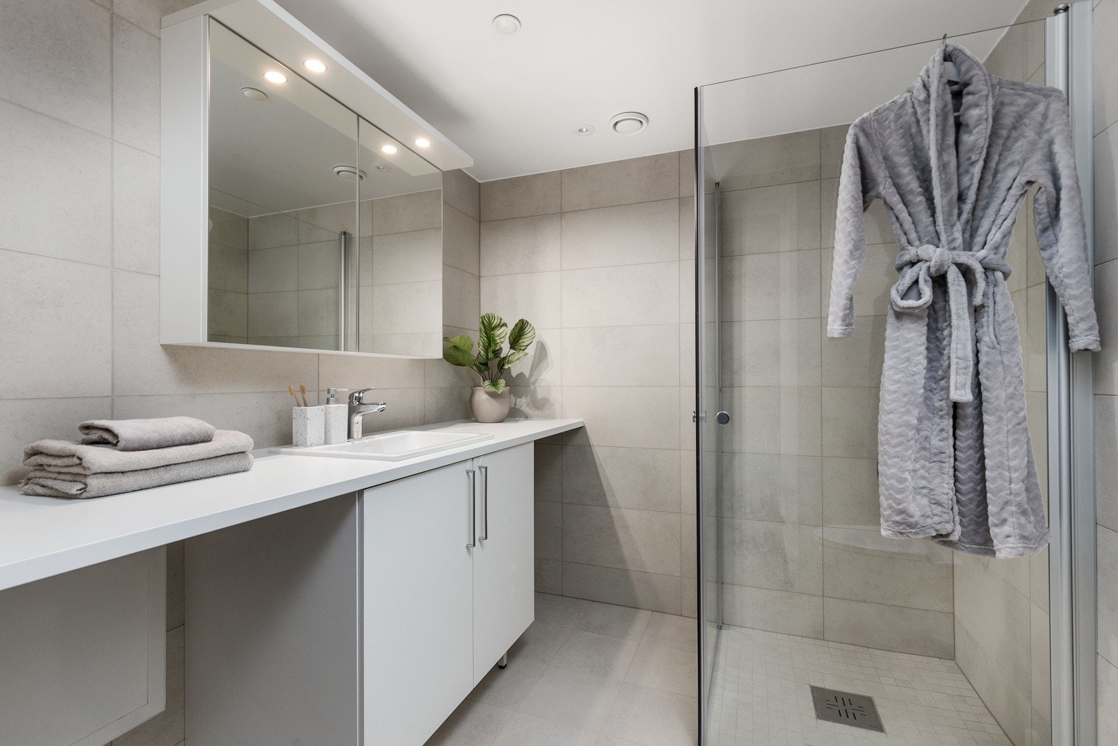 Delikat flislagt bad med vegghengt toalett, dusjsone med innfellbare dører samt servant med skapinnredning. Galleribilde