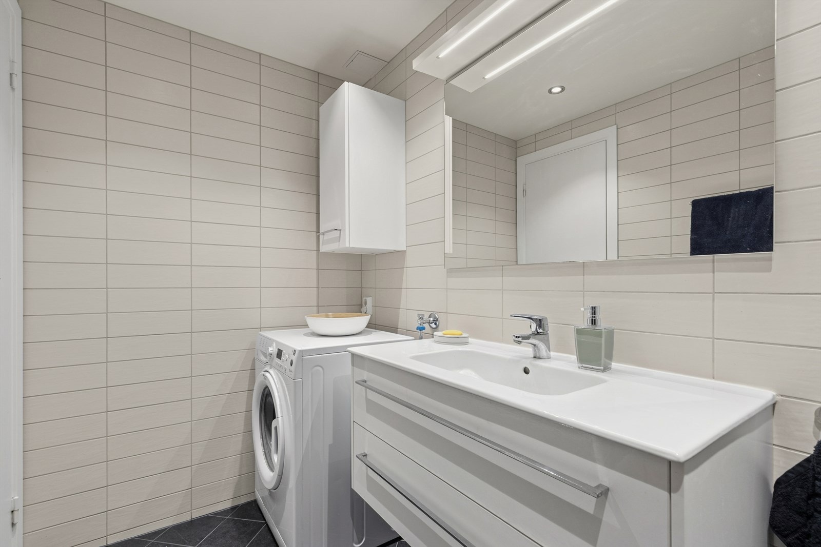 Flislagt bad/wc med servantskap, speil, vegghengt toalett, svingbare dusjdører og opplegg til vaskemaskin/tørketrommel. Galleribilde