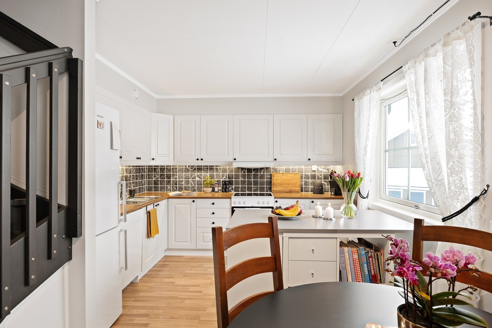 Kjøkkenet har en pen innredning med profilerte hvite fronter, laminert benkeplate og fliser over benken. Galleribilde