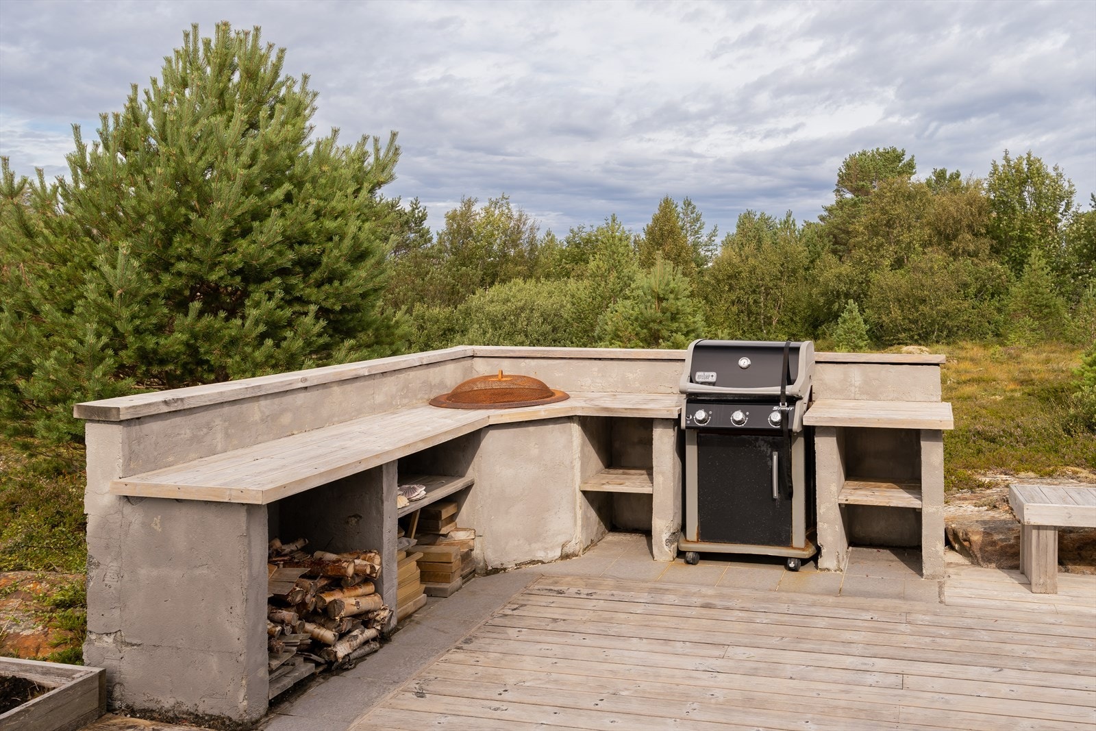Utendørs kjøkkenområde med plass til gassgrill og rikelig benkeplass. Integrerte hyller gir praktisk oppbevaring av ved og utstyr. Galleribilde