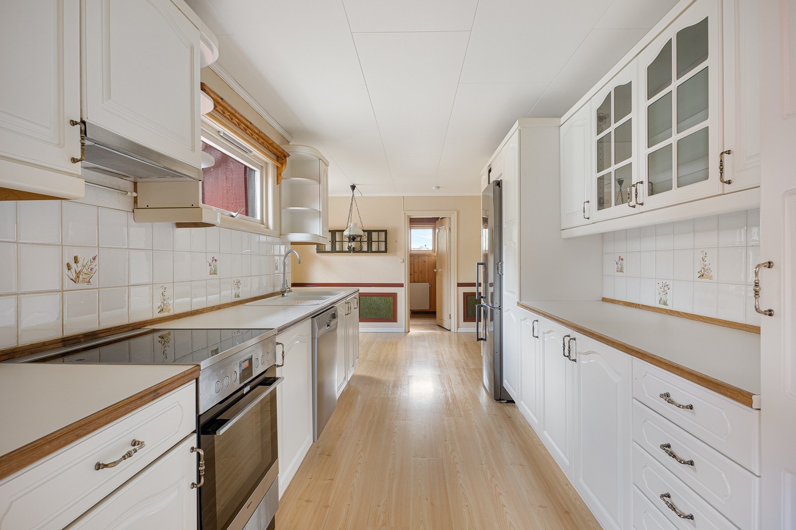 Kjøkkenet ligger i eget rom og har god plass til spisebord i enden av innredningen. Innredningen er montert langs to parallelle vegger og har hvite fronter, vitrineskap, laminatbenkeplater og fliser på veggen. Galleribilde