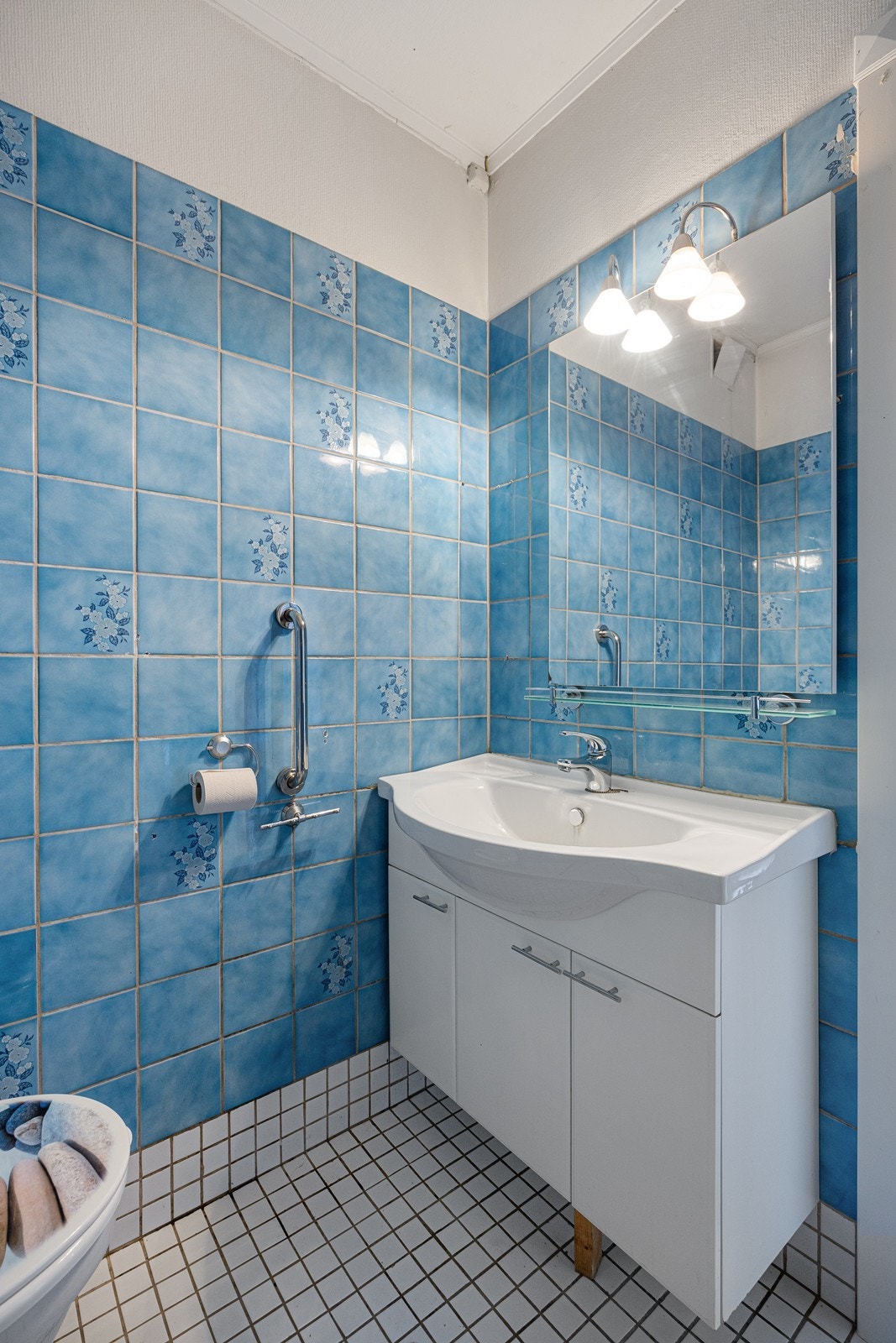 Det flislagte badet er utstyrt med hvit innredning, gulvmontert toalett, åpent dusjhjørne og opplegg for vaskemaskin. Galleribilde