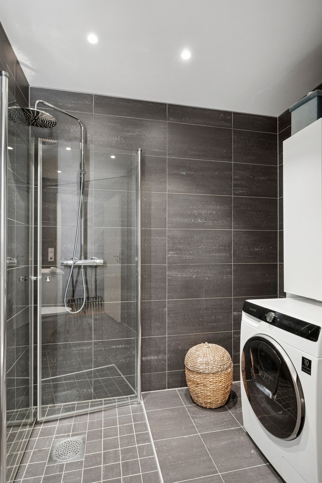 Badet har vegghengt toalett, dusjhjørne, servant med oppbevaring og opplegg for vaskemaskin. Galleribilde