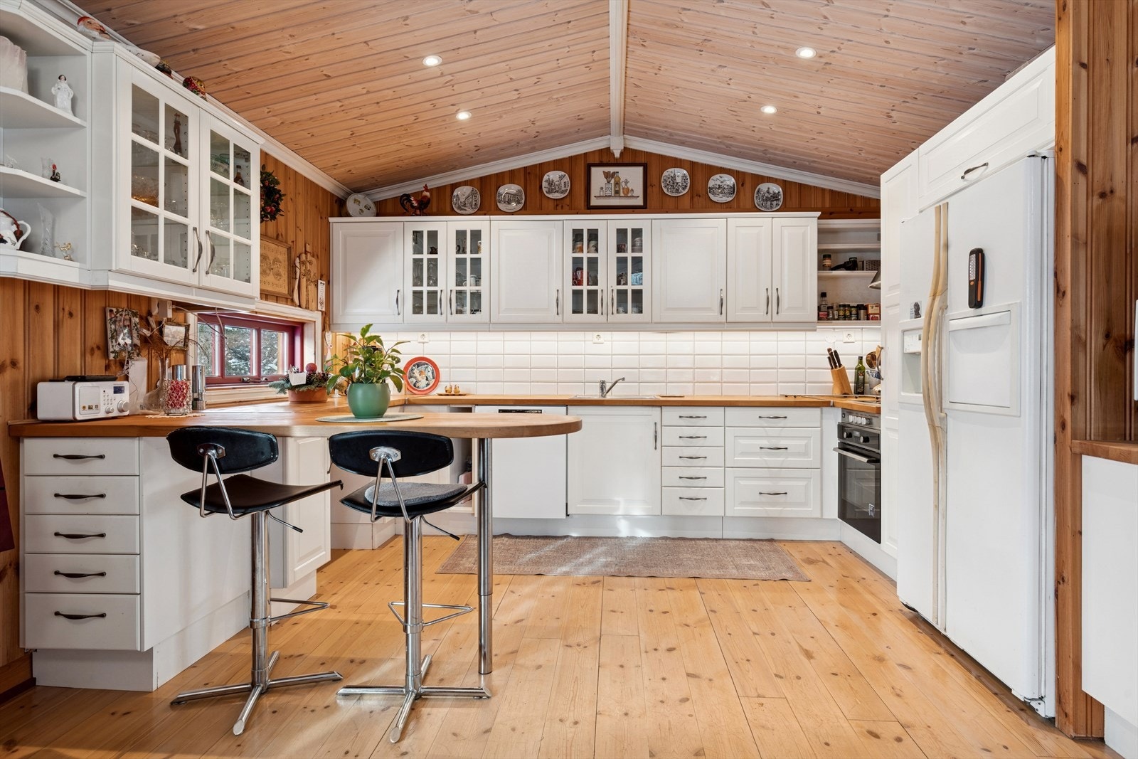 Stort og innbydende kjøkken med hvit og lys innredning som harmonerer vakkert med boligens solide tømmervegger. Galleribilde