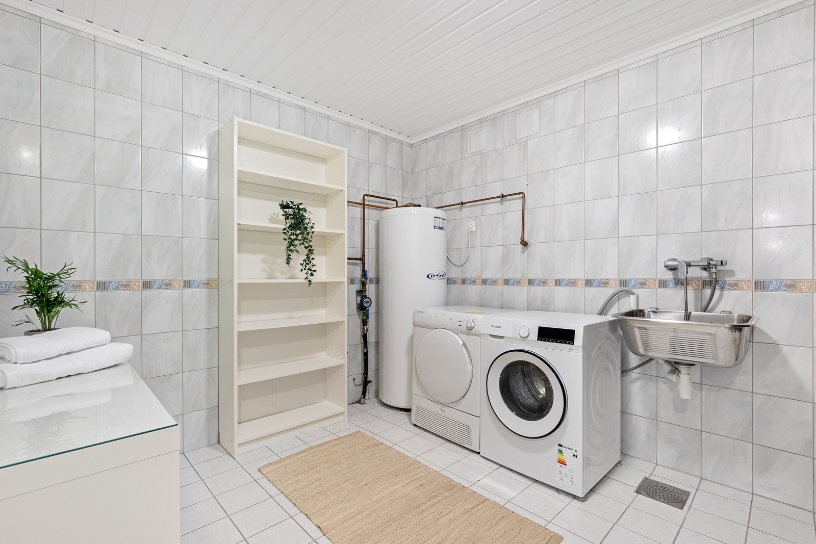 Romslig, separat vaskerom med flislagte overflater, utslagsvask og opplegg for vaskemaskin. Galleribilde