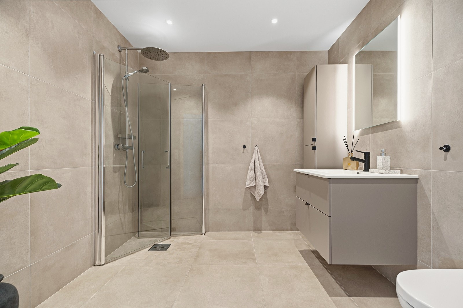 Lekkert bad med flislagte overflater, innredet med toalett, nedfelt servant og dusjhjørne med innfellbare dører Galleribilde