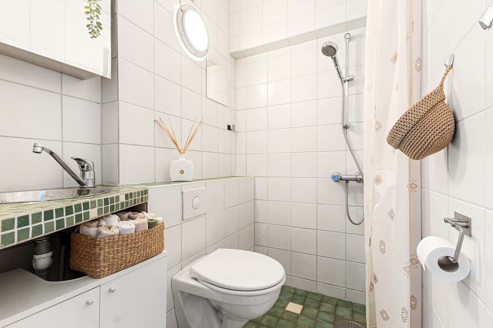 Praktisk bad som er flislagt og ligger i tilknytning til entréen, innredet med dusjhjørne, vegghengt toalett, servant med tilhørende innredning og speilskap. Galleribilde