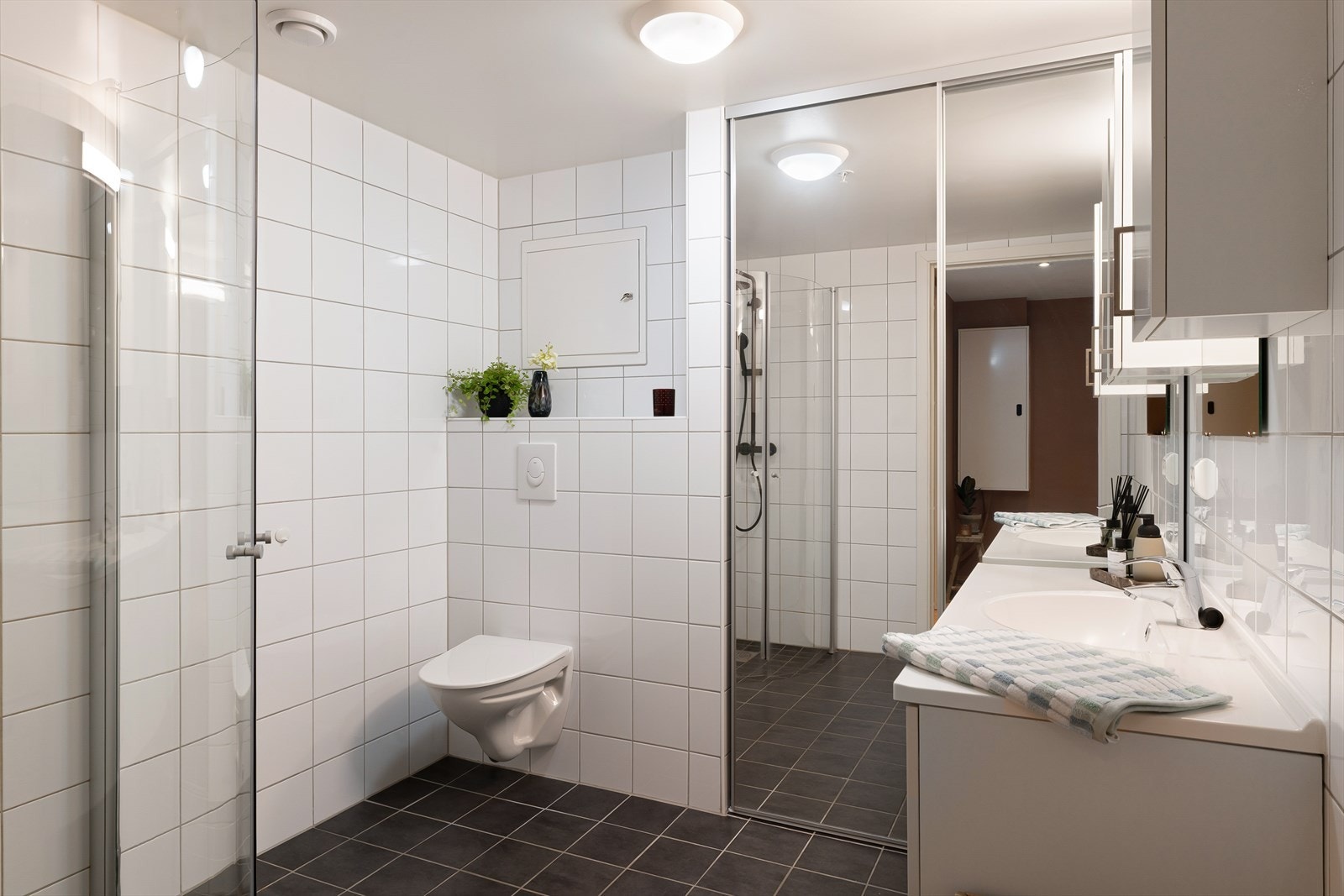 Lyst og helfliset bad med dusjhjørne, vegghengt toalett og vaskeromsløsning. Galleribilde
