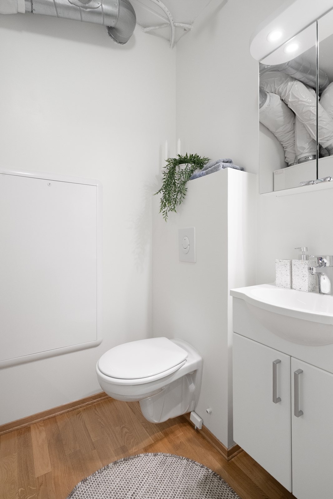 Bod/teknisk rom i leiligheten er innredet med vegghengt toalett, smalt servantskap og speilskap med belysning. Galleribilde