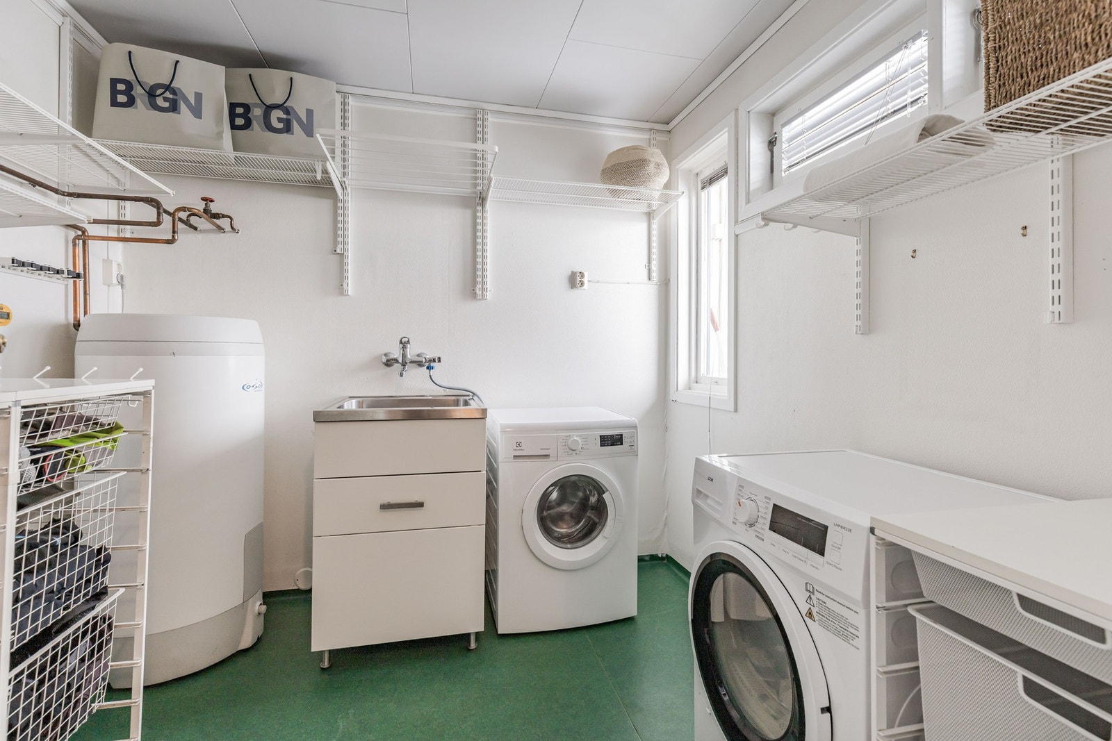 Praktisk vaskerom med belegg på gulv og malte vegger. Rommet er innredet med skyllekar, varmtvannstank og opplegg for vaskemaskin. Galleribilde