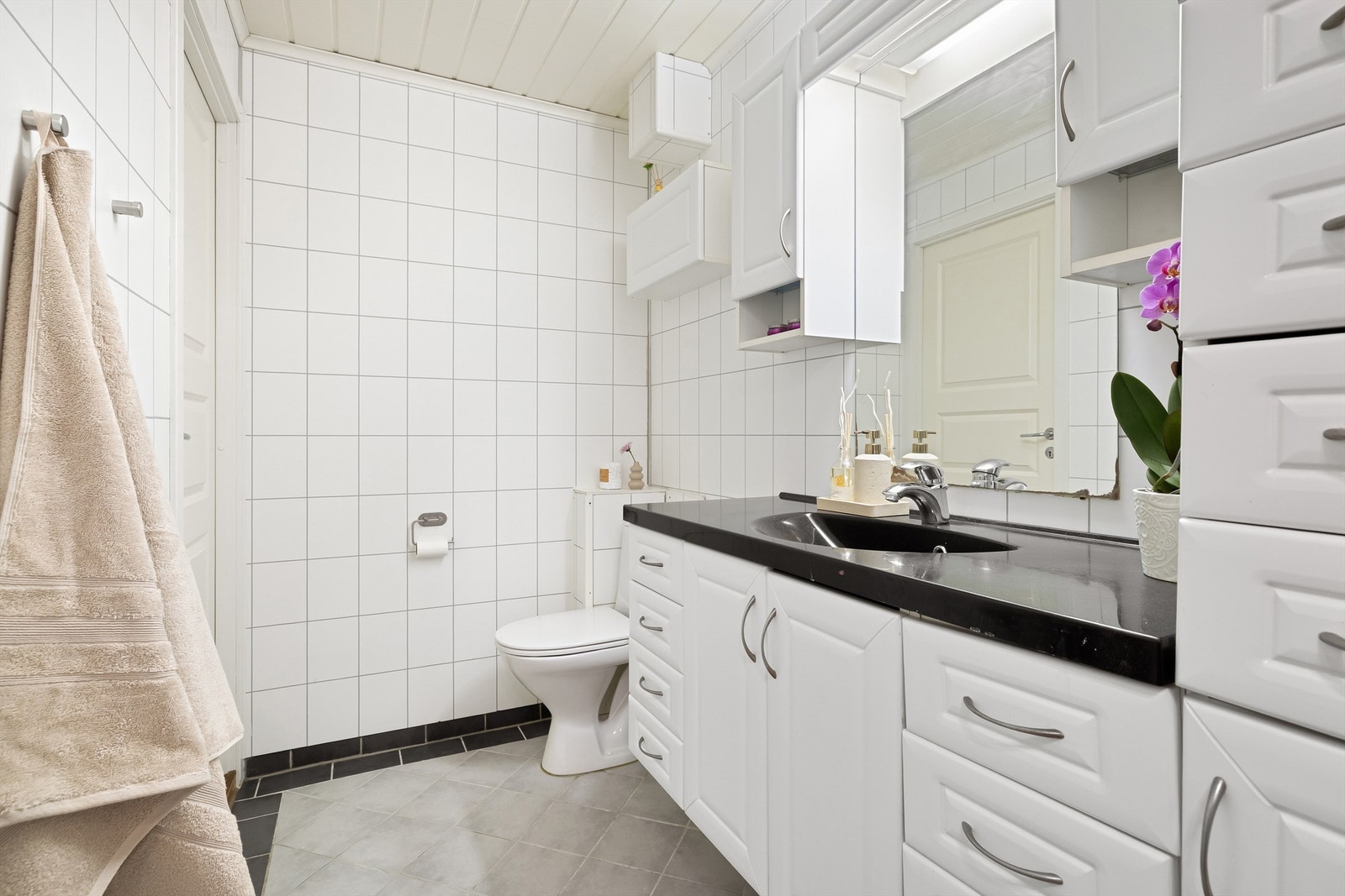 Badet inneholder vegghengt servantinnredning, servant med armatur, speilskap med lys og stikkontakt, vegghengt skap, dusjhjørne med glassdører og gulvstående toalett. Galleribilde