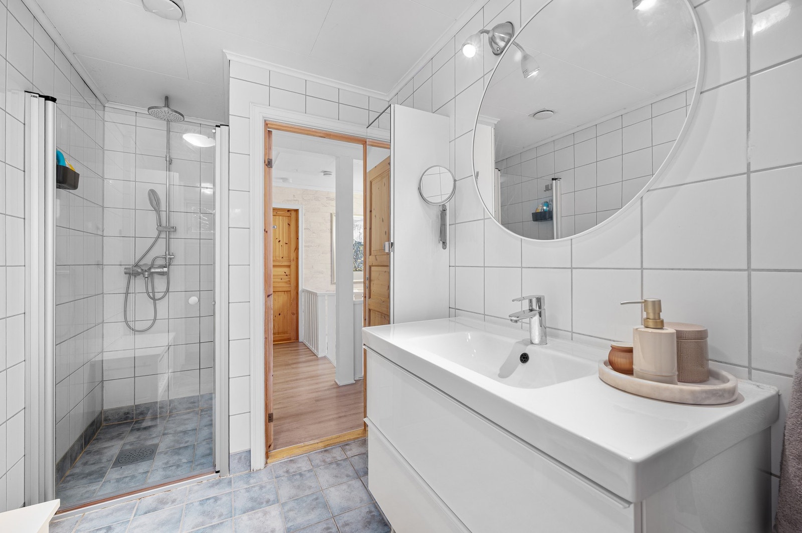 Badet er innredet med veggmontert servant, dusjnisje med glassdør, speil og skap. Galleribilde