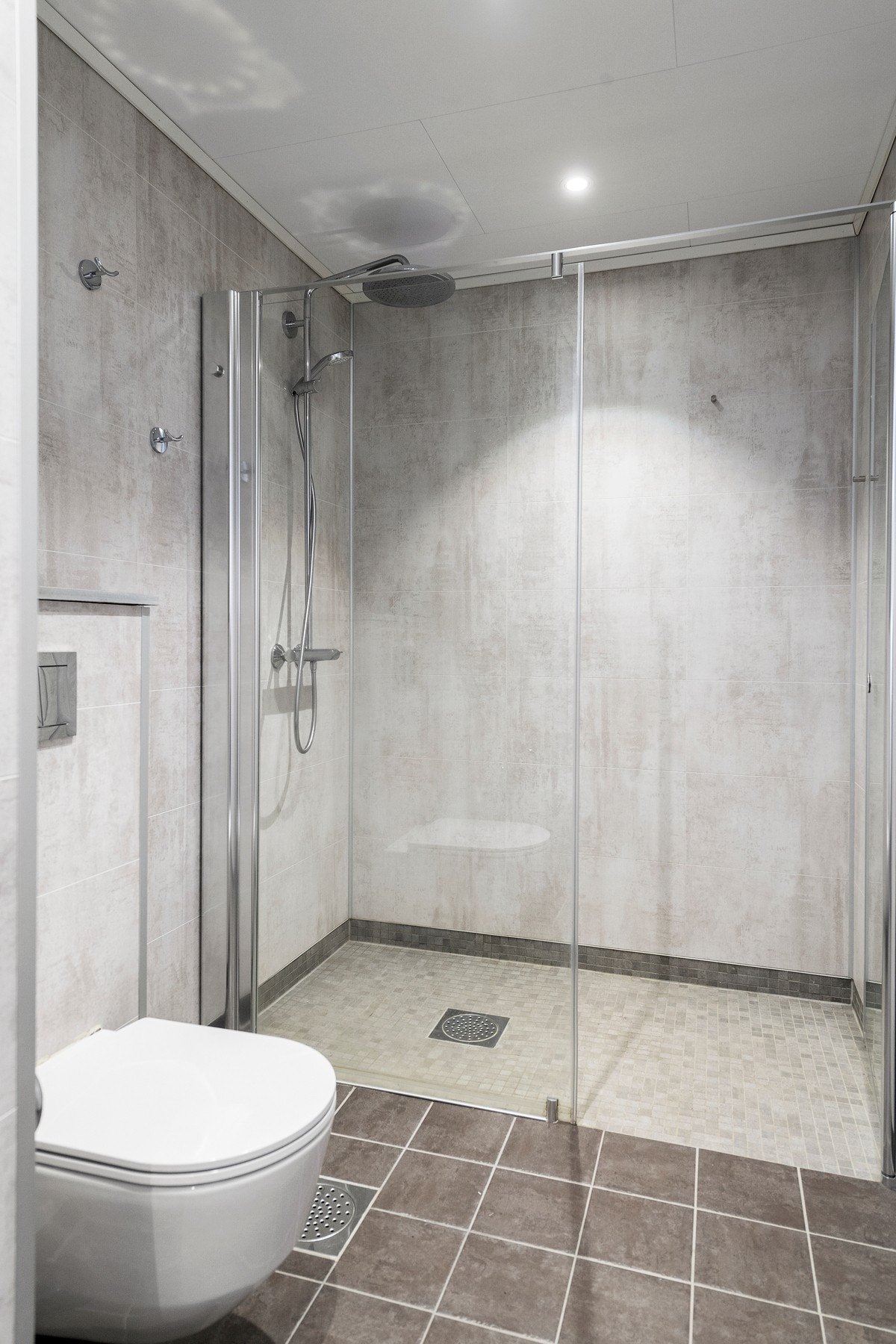 Badet er innredet med heldekkende servant, vegghengt toalett og et større dusjhjørne med glassvegg. Galleribilde