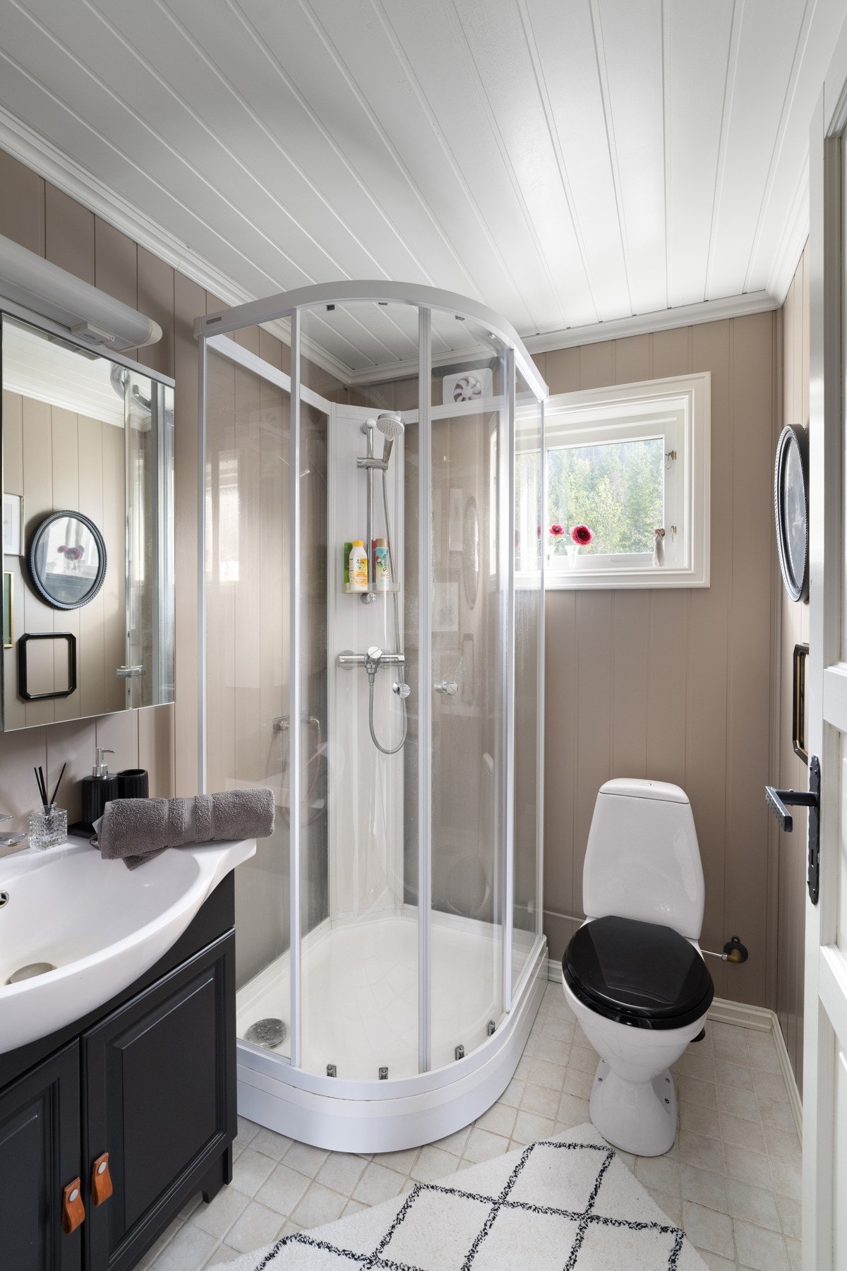 Bad med fliser på gulv og panel på vegg. Innredning med servant, toalett og dusjkabinett. Galleribilde