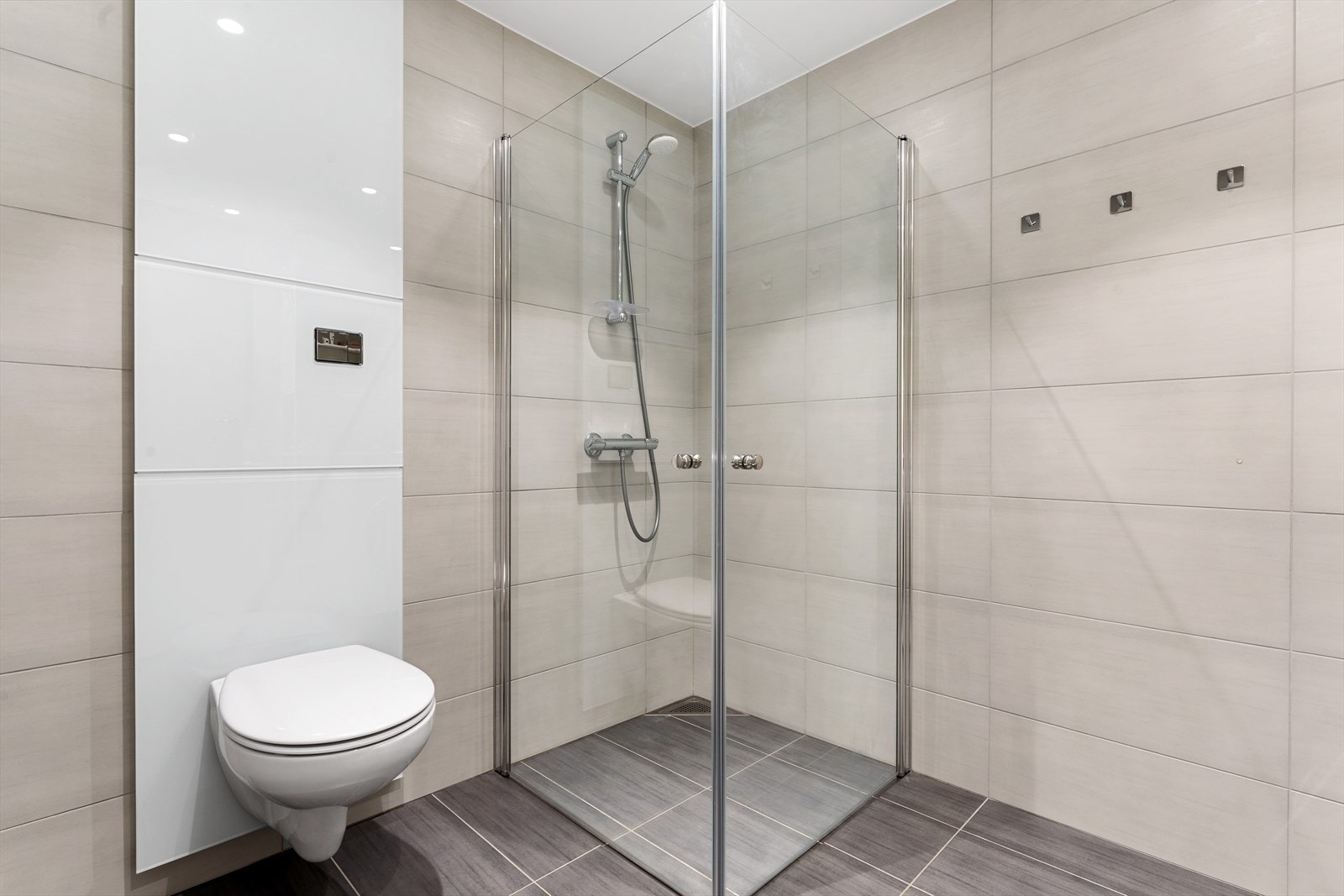 Badet er flislagt og utstyrt med nedfelt servant, veggmontert toalett, dusjvegger og opplegg for vaskemaskin. Galleribilde