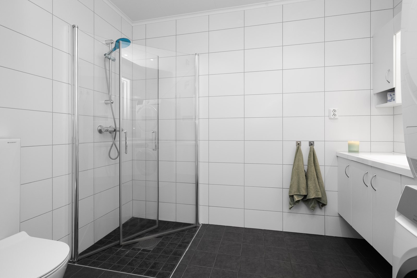 Lyst og romslig, flislagt baderom utstyrt med elektriske varmekabler i gulv, vegghengt toalett og dusjhjørne. Galleribilde