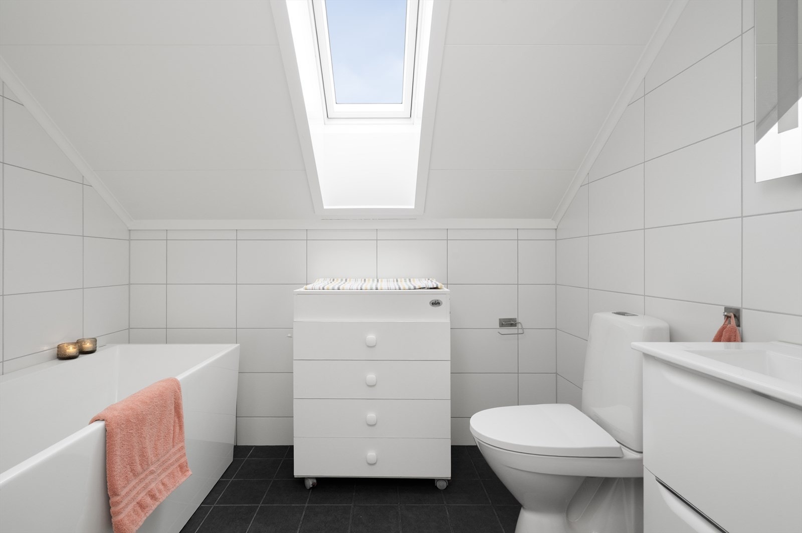 Pent baderom med flis på gulv med varmekabler, flis på vegg og malte takessplater i tak. Det er gulvmontert toalett og badekar. Galleribilde