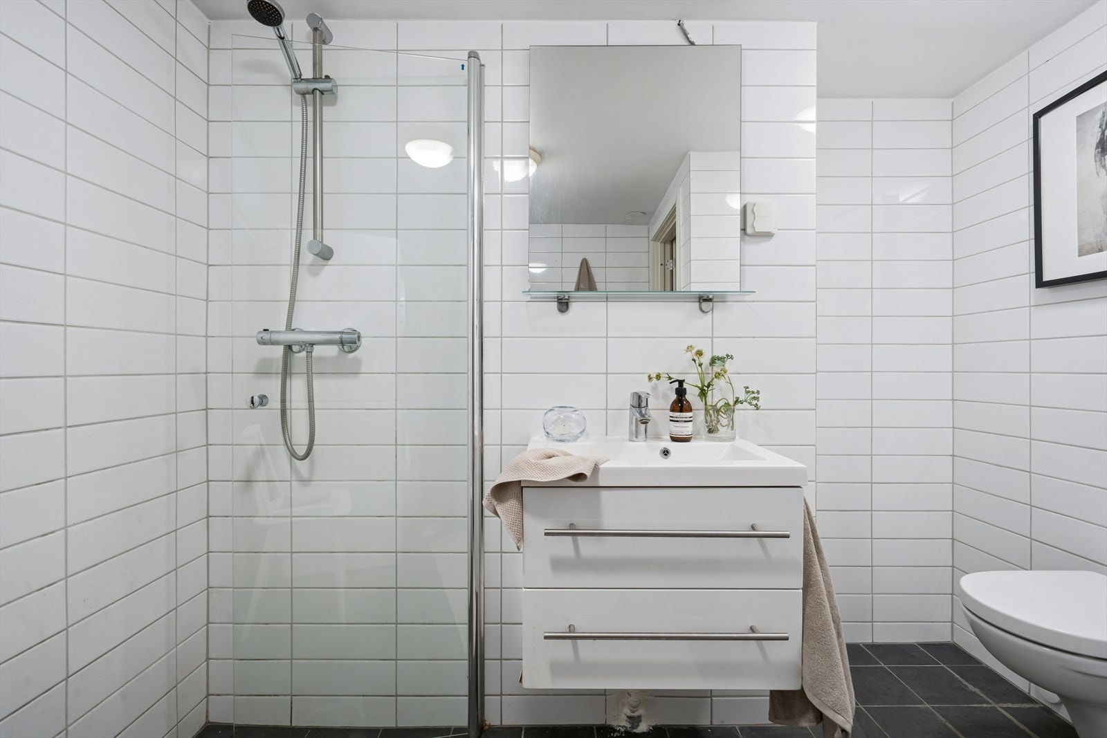 Flislagt baderom fra 2016. Baderommet er innredet med servantinnredning med speil, toalett og dusjhjørne. Varmekabler i gulv. Galleribilde