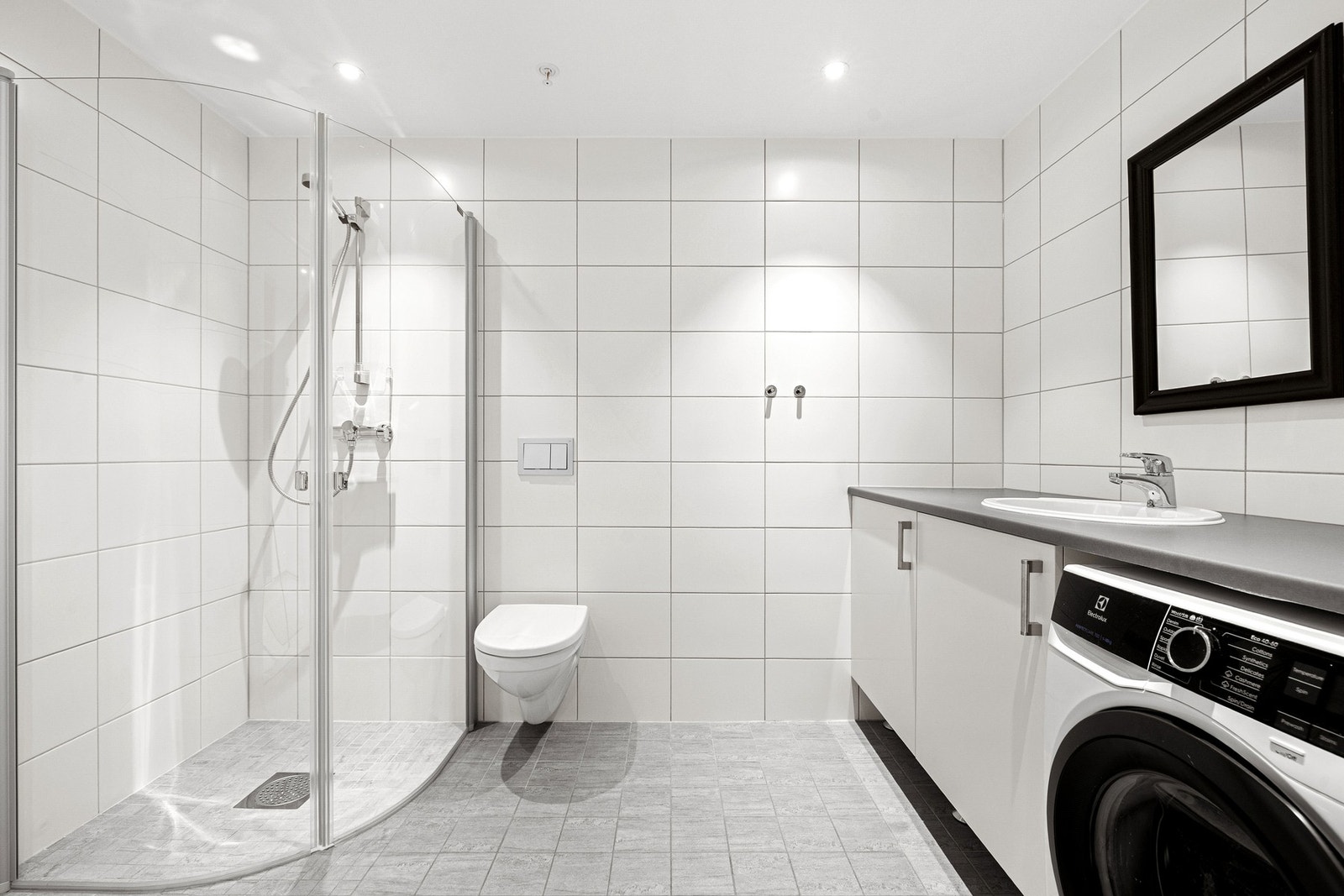 Praktisk bad/vaskerom 5,6 kvm. Utstyrt med opplegg for vaskemaskin, veggmontert toalett, innfellbare dusjdører, vannfordelerskap og benkeskap med servant. Galleribilde