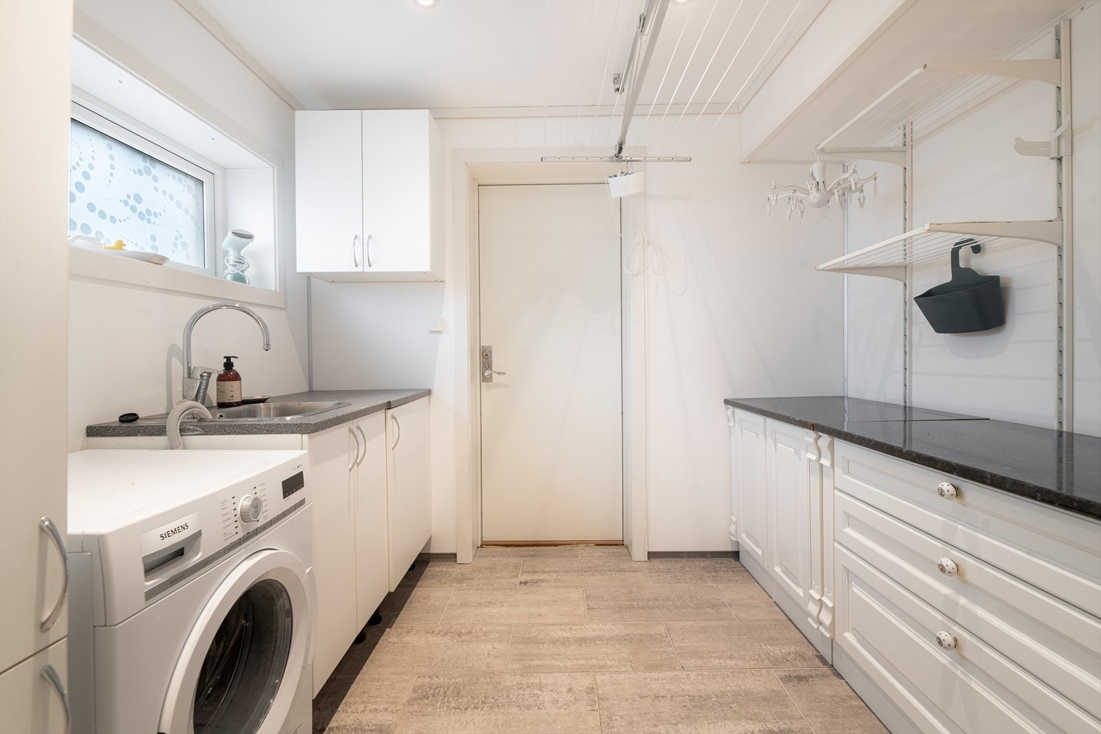 Vaskerommet er innredet med servantinnredning med benk, skuffer og skap, samt opplegg for vaskemaskin. Rommet har flis med varmekabler på gulv og baderomsplater på vegger. Galleribilde