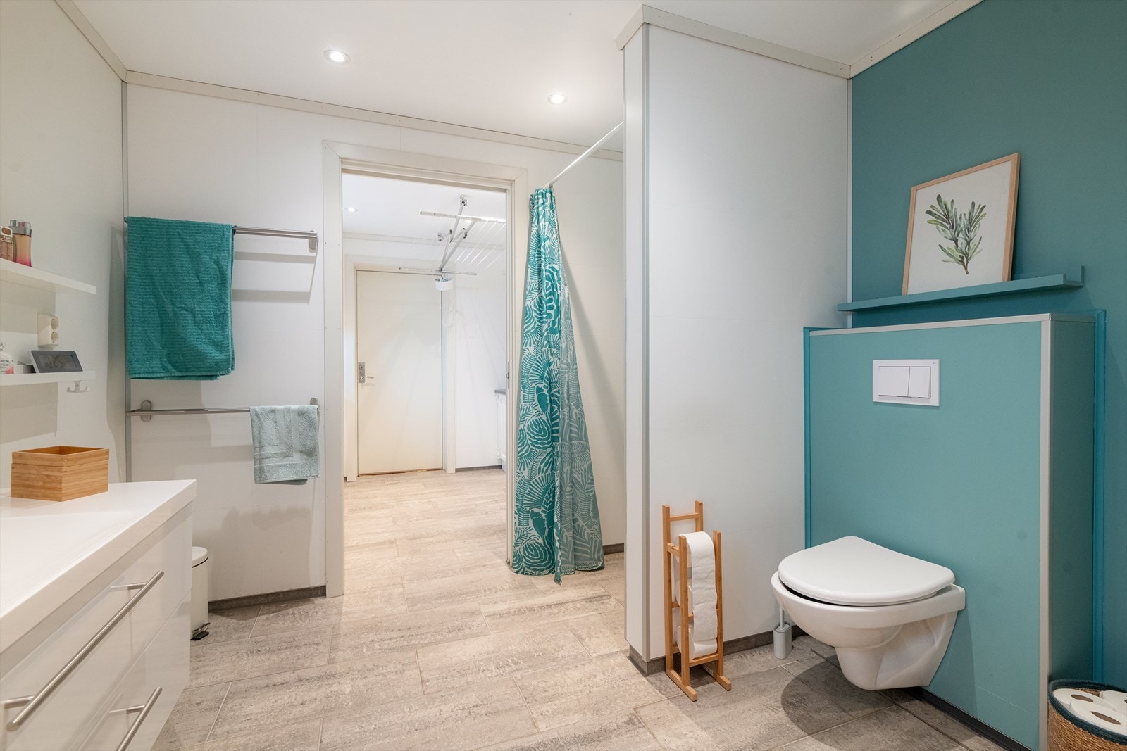 Delikat bad av god størrelse, innredet med veggmontert toalett, dusj på vegg og servantinnredning med skuffer og speil. Galleribilde