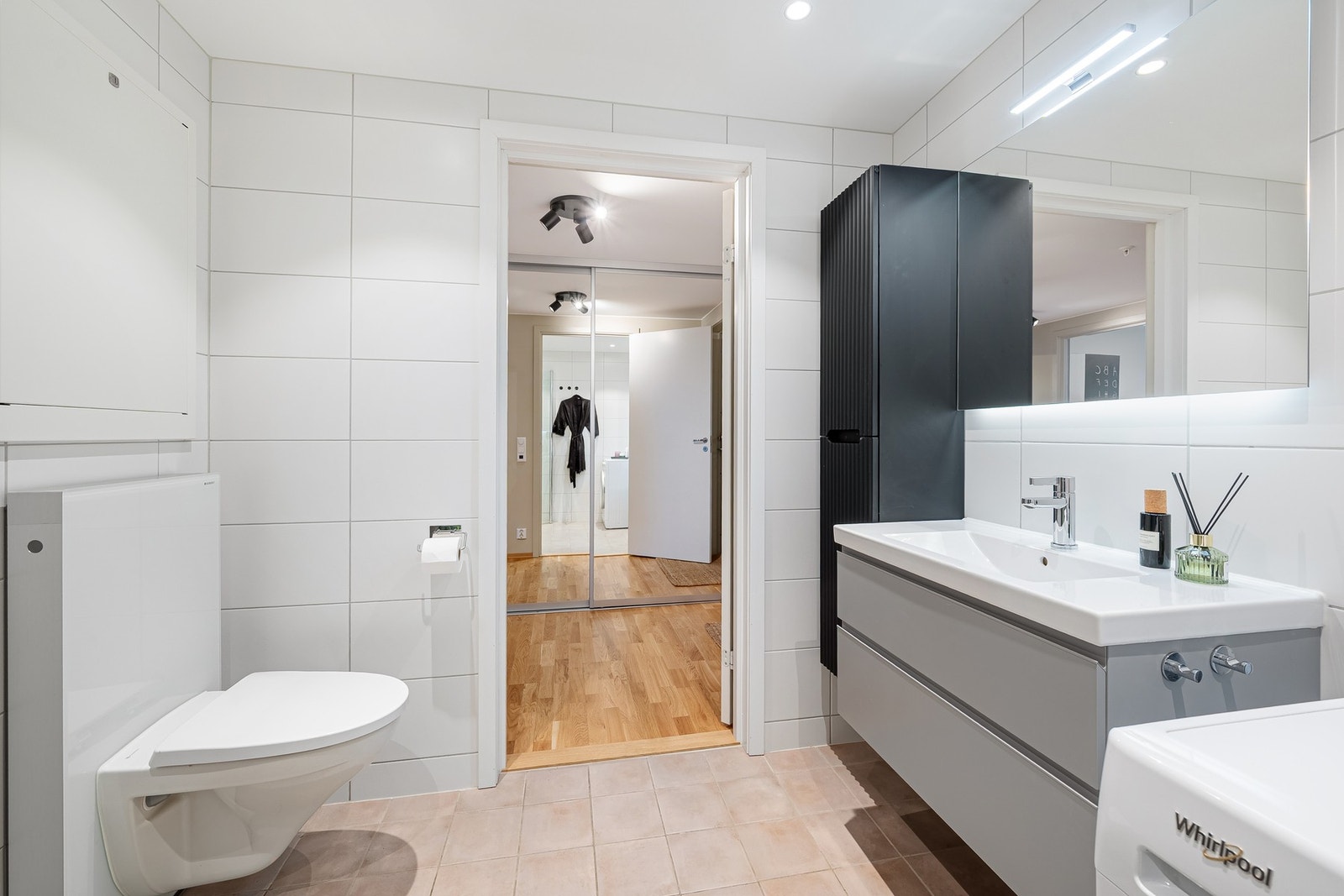 Badet er innredet med veggmontert toalett, dusjhjørne, servantinnredning, veggmontert høyskap og speil med belysning. Galleribilde