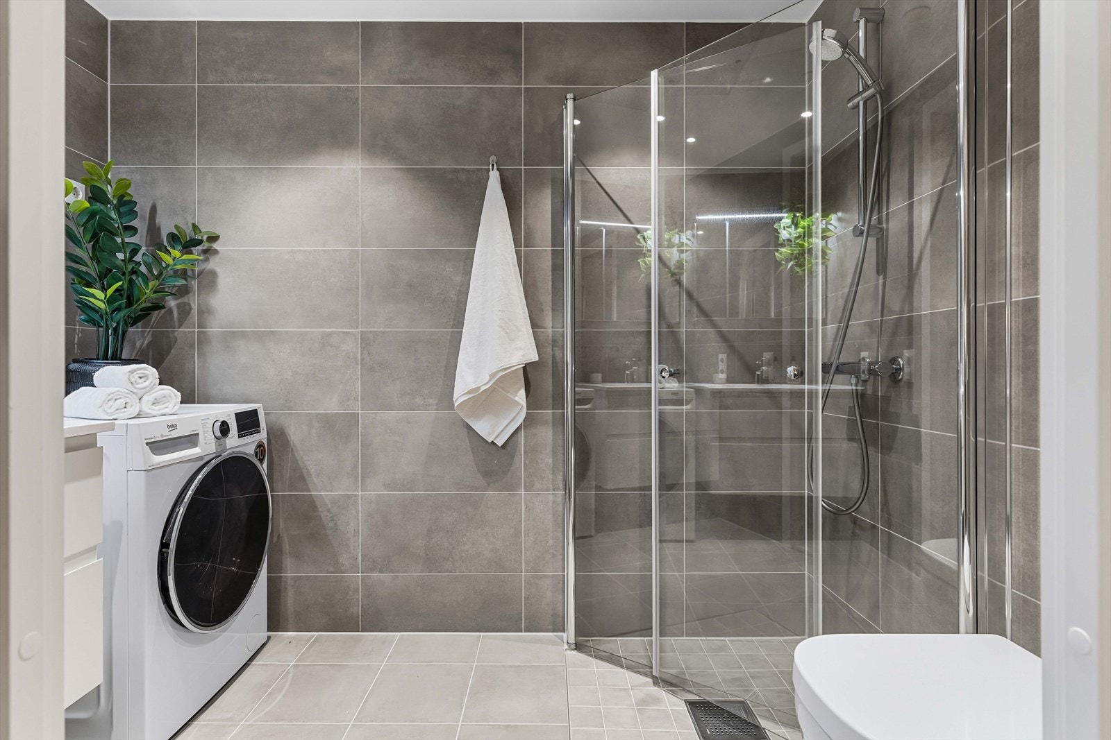 Delikat baderom med dusjhjørne i glass og god oppbevaringsplass i servantinnredning. Tidløse materialvalg og praktisk planløsning. Galleribilde