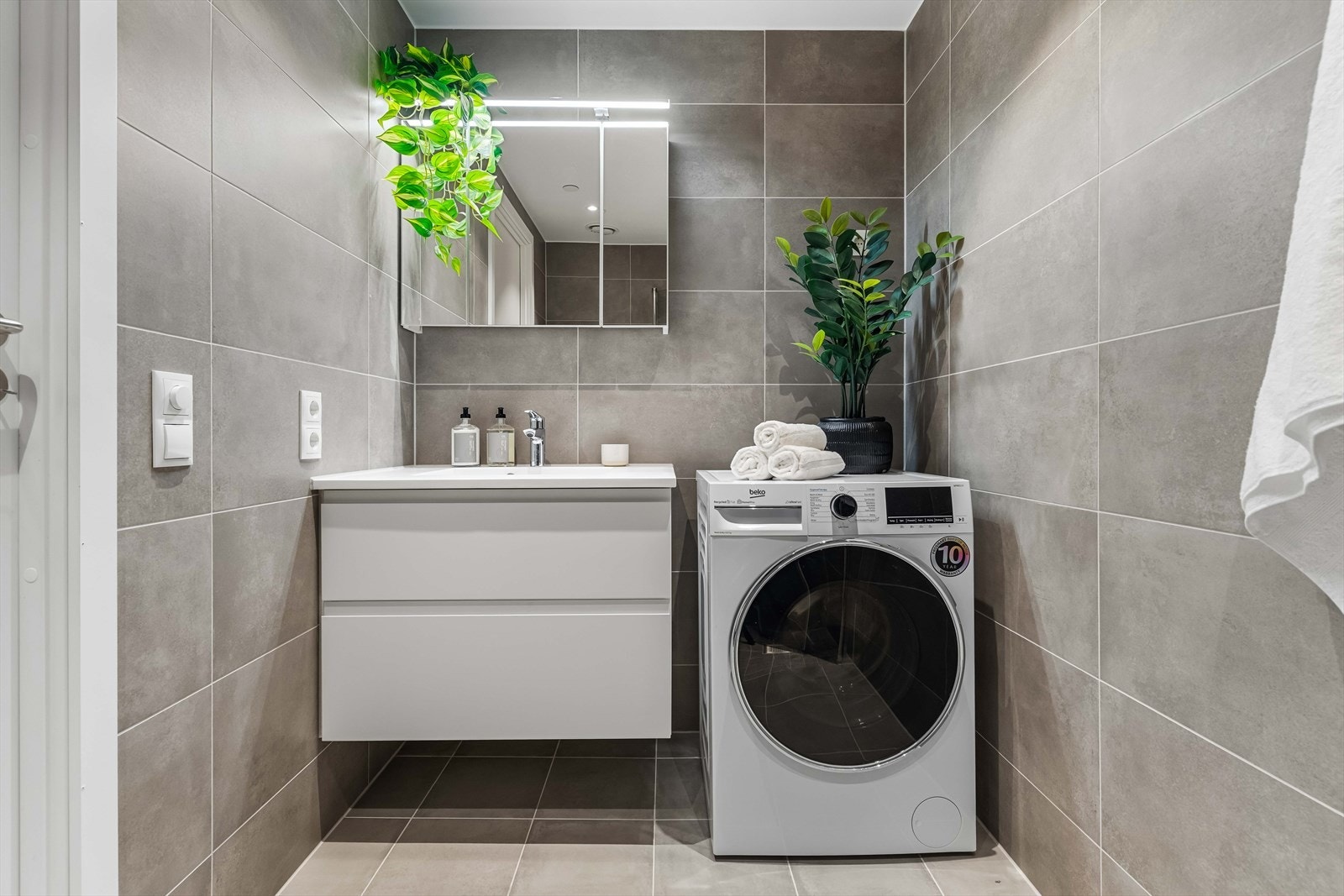 Flislagt bad med moderne uttrykk og stilrene detaljer. Egen opplegg for vaskemaskin gir ekstra komfort i hverdagen. Galleribilde