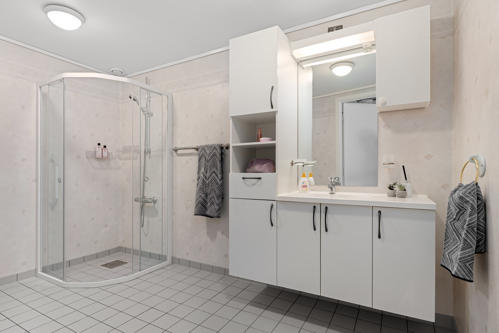 Stort bad med fliser på gulv og tapetserte vegger. Servant med mye skapplass. Galleribilde