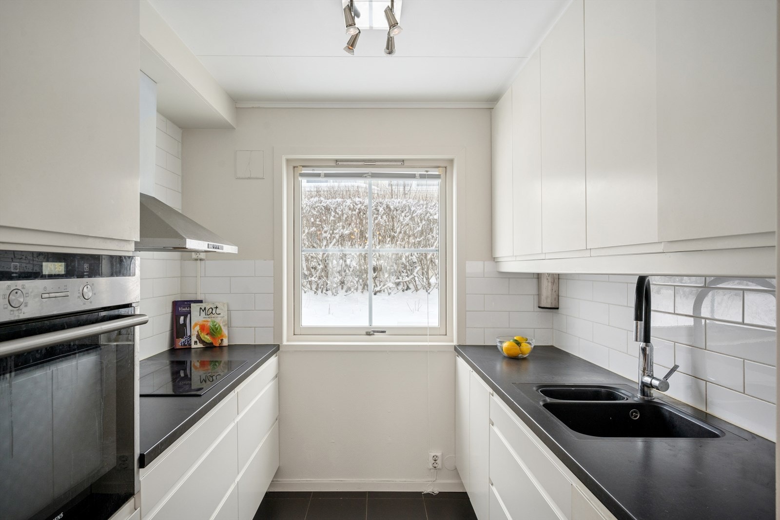 Her får du en praktisk kjøkkenløsning med integrert koketopp, kjøkkenvifte montert fra taket og stekeovn, samt en laminert benkeplate med nedfelt vask i kompositt -både pent og praktisk. Galleribilde