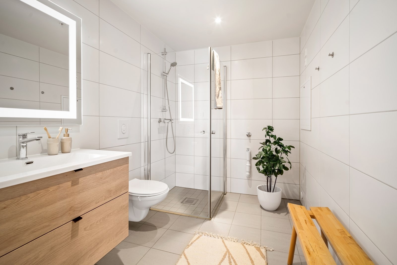 Badet er helfliset og utstyrt med dusjhjørne, vegghengt klosett og servant med innredning. Galleribilde